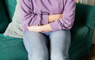 A woman wearing a purple jumper and jeans sat on a sofa holding her stomach
