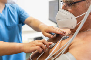 Close-up of a male doctor attaching electrodes on patient's chest to monitor electrocardiogram in hospital.