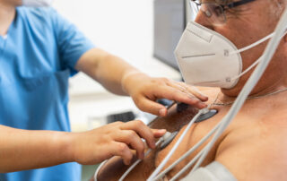 Close-up of a male doctor attaching electrodes on patient's chest to monitor electrocardiogram in hospital.