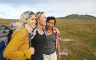 A group oF female hiking friends huddle together on a rocky moorland in the countryside.