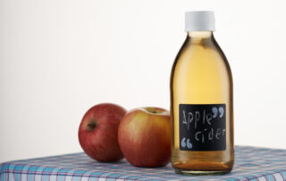 A bottle of apple cider vinegar next to apples on a table