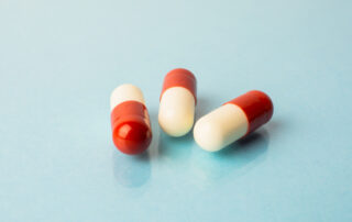 Three red and white capsule pills laying on a flat blue surface