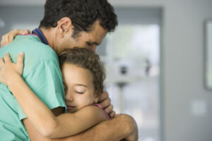 A doctor wearing his teal hospital scrubs hugging his daughter