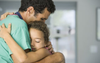 A doctor wearing his teal hospital scrubs hugging his daughter
