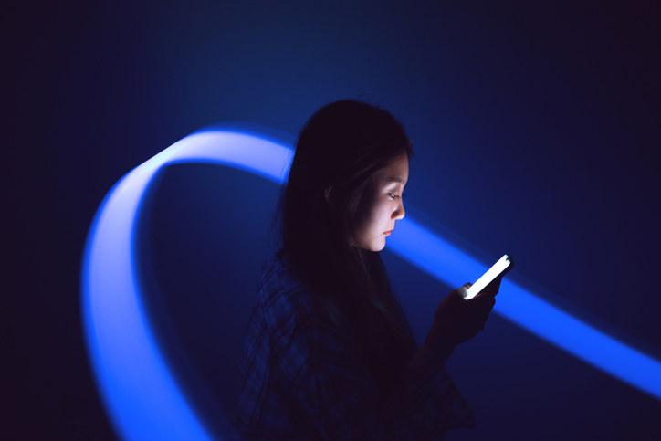 A woman looking at the bright light from her phone in a dark room