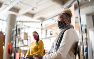 Two women sat in a large room with 2 metres between them whilst wearing masks at a rehabilitation group session