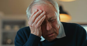 An older man holding his head and looking distressed experiencing delirium symptoms