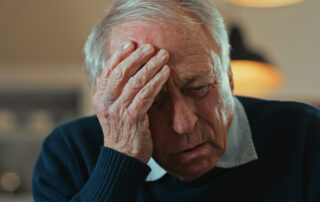 An older man holding his head and looking distressed experiencing delirium symptoms