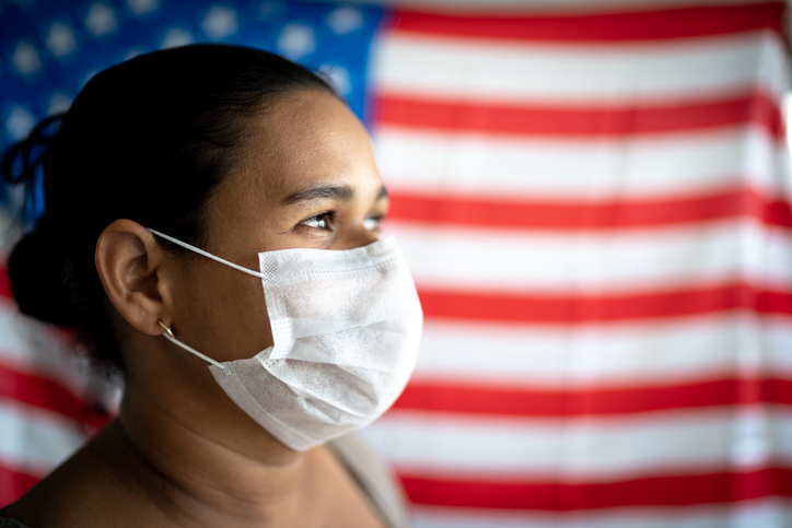 Woman wearing a face mask stood infront of the US flag