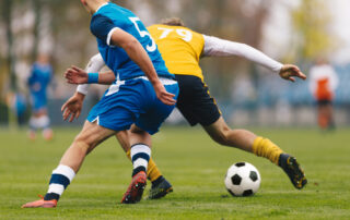 Football Players in Blue and Yellow Jersey Uniforms Running with a football on Grass Pitch