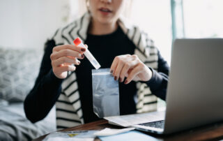Cropped shot of young Asian woman consulting to her family doctor online in a virtual appointment holding a medical test tube conducting Covid-19 diagnostic test at home