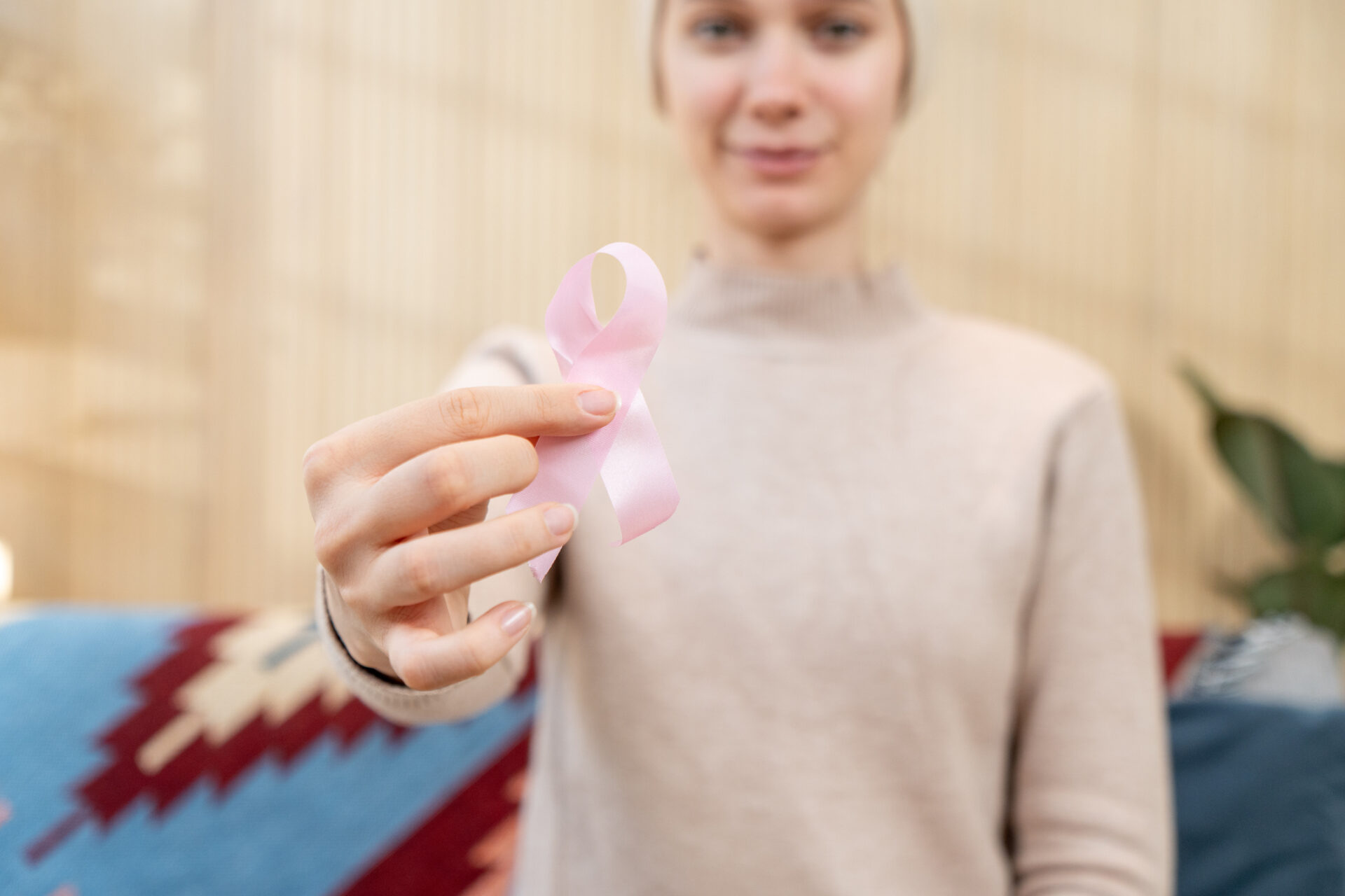 A woman adult with a bald head is holding a pink cancer awareness ribbon symbolizing support for a cause