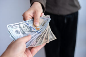 Cropped shot view of someone giving America dollar banknotes to other person - BMJ Group