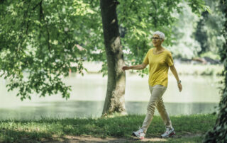 Older woman with grey hair, walking by a lake with trees
