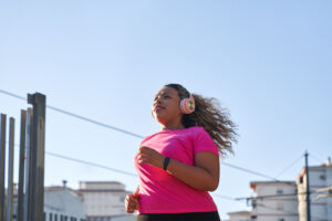 Woman in pink top and headphones running in a city