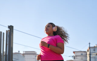 Woman in pink top and headphones running in a city