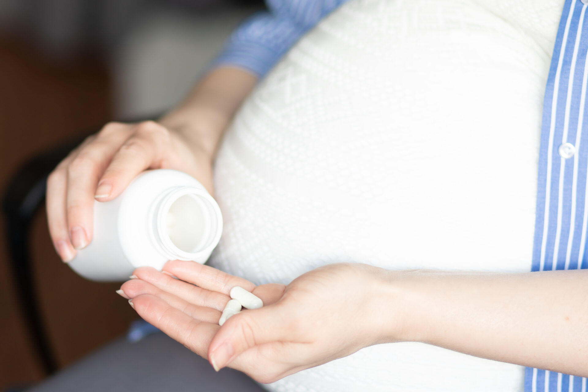 pregnant woman sits in a chair at home holding a jar of pills in her hands