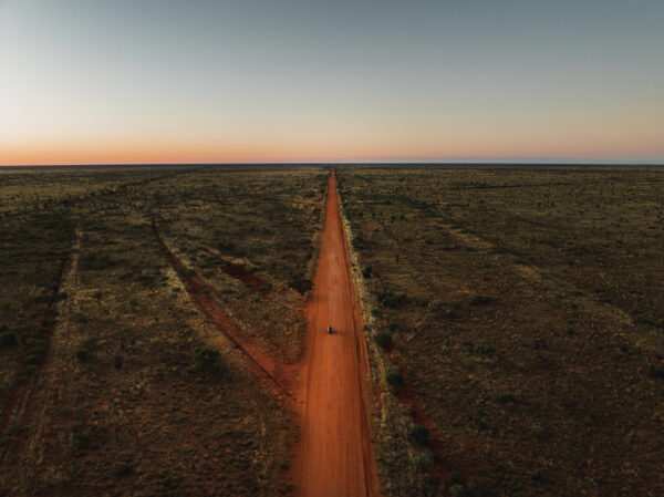 Tranquil scene showing a vehicle driving on a a remote dirt road in the Tanami Desert shot from an aerial point of view at sunset Northern Territory Australia