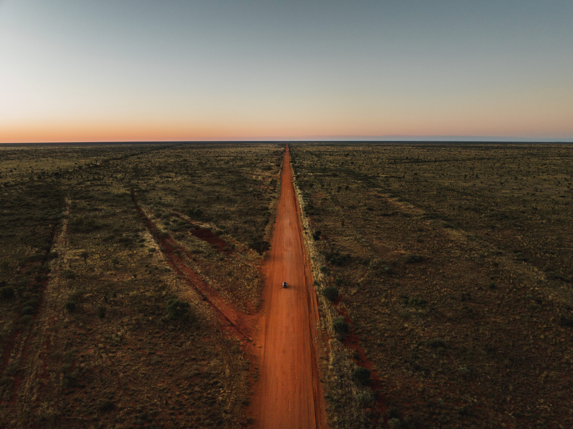 Tranquil scene showing a vehicle driving on a a remote dirt road in the Tanami Desert shot from an aerial point of view at sunset Northern Territory Australia