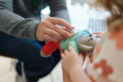 Pediatrician and little girl treat teddy bear in hospital
