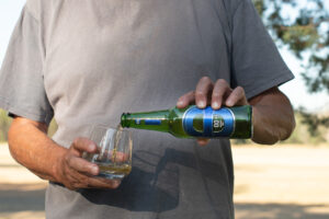 Man pouring a bottle of blue label 00 alcohol free beer into a glass on a hot sunny day