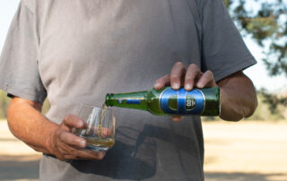 Man pouring a bottle of blue label 00 alcohol free beer into a glass on a hot sunny day