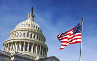 U.S. Capitol dome with an American flag waving on a clear blue sky.