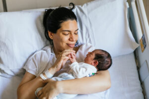 Mother lying in a hospital bed cradling her newborn and smiling at the baby, tender moment in a hospital room.