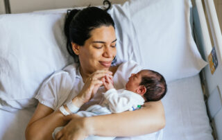 Mother lying in a hospital bed cradling her newborn and smiling at the baby, tender moment in a hospital room.