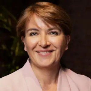 Smiling woman with short light brown hair wearing a pale pink blazer, facing the camera.