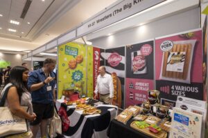 Exhibition booth for Westlers sausages with colorful banners, samples on a table, and attendees chatting at a trade show show floor.