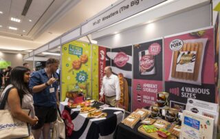 Exhibition booth for Westlers sausages with colorful banners, samples on a table, and attendees chatting at a trade show show floor.