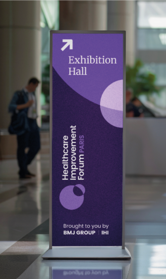 Purple exhibition-hall sign in a modern lobby with an up-right arrow, reading 'Exhibition Hall' for the Healthcare Improvement Forum Paris.