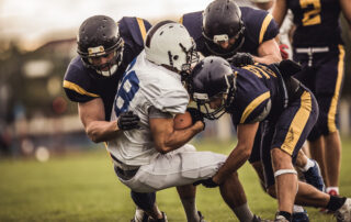 Rugby players in navy and gold uniforms collide in a tightly packed scrum on a grassy field, white jersey visible in the center.