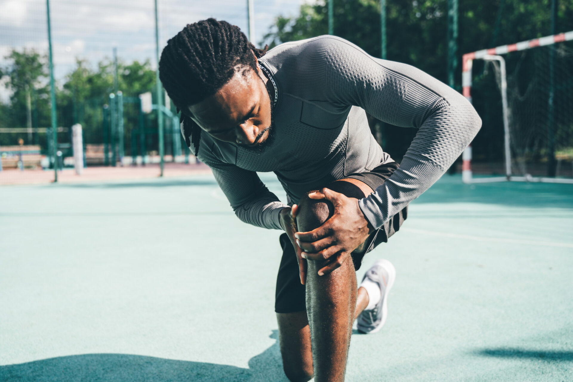 Athlete in a gray textured shirt bending to stretch his leg on an outdoor sports court.