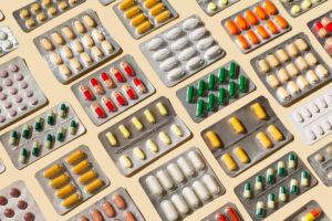 Assorted blister packs of pills in various colors scattered on a light background.