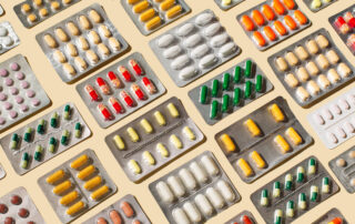 Assorted blister packs of pills in various colors scattered on a light background.