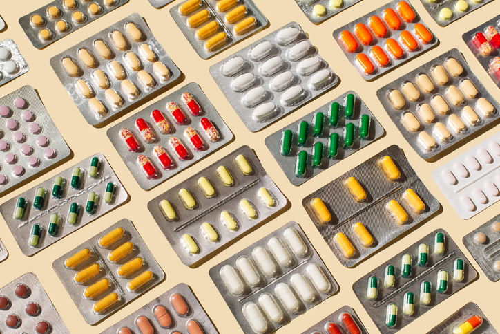 Assorted blister packs of pills in various colors scattered on a light background.