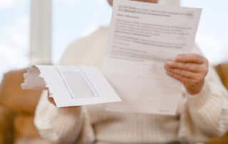 Person holding a printed letter with a torn white envelope visible in the foreground; the background is soft-focused.