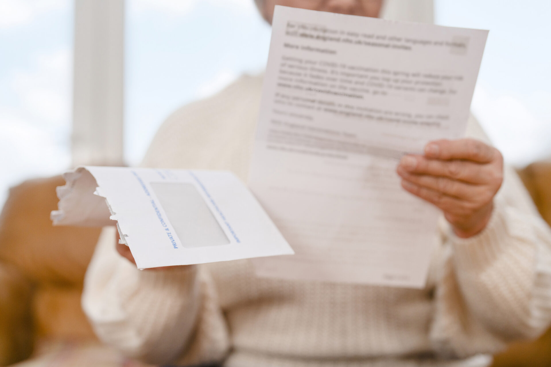 Person holding a printed letter with a torn white envelope visible in the foreground; the background is soft-focused.