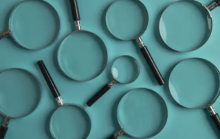 Several teal frying pans of different sizes arranged on a teal surface.