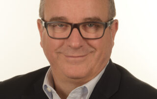 Head-and-shoulders portrait of a smiling man in glasses and a suit, looking at the camera.