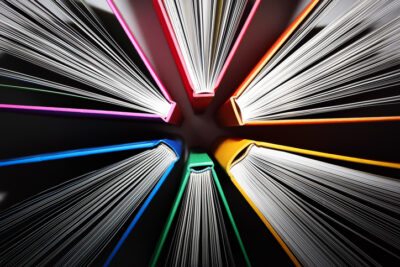 Top-down view of colorful hardcover books arranged in a circle with pages fanned outward.