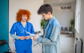 Male patient in a denim jacket reviews documents with a nurse in blue scrubs in a clinic.