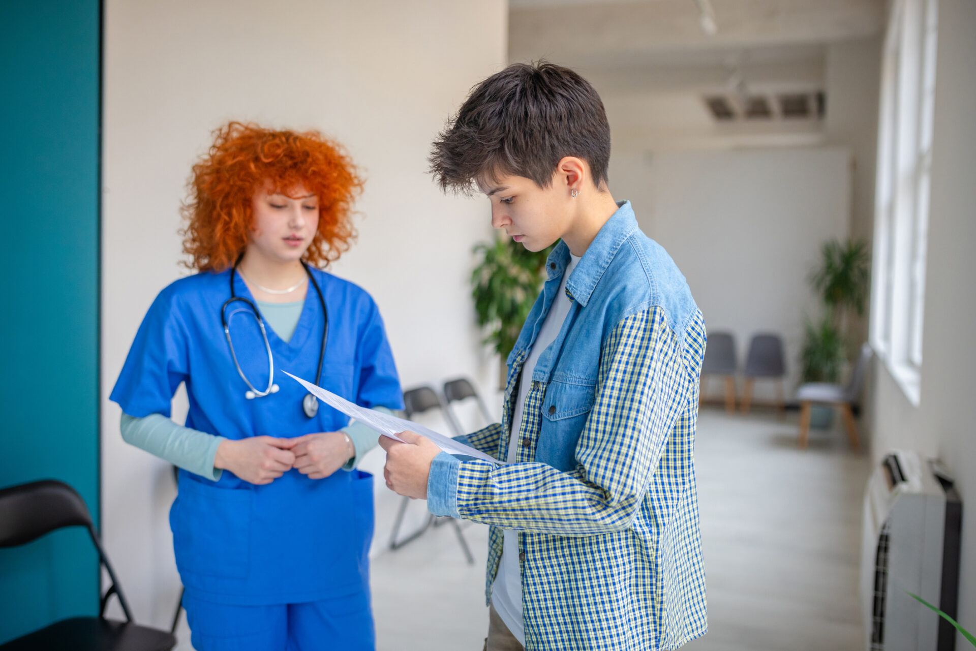 Male patient in a denim jacket reviews documents with a nurse in blue scrubs in a clinic.