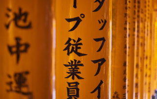 Close-up of orange wooden pillars with vertical black Japanese kanji inscriptions, lined in a row.