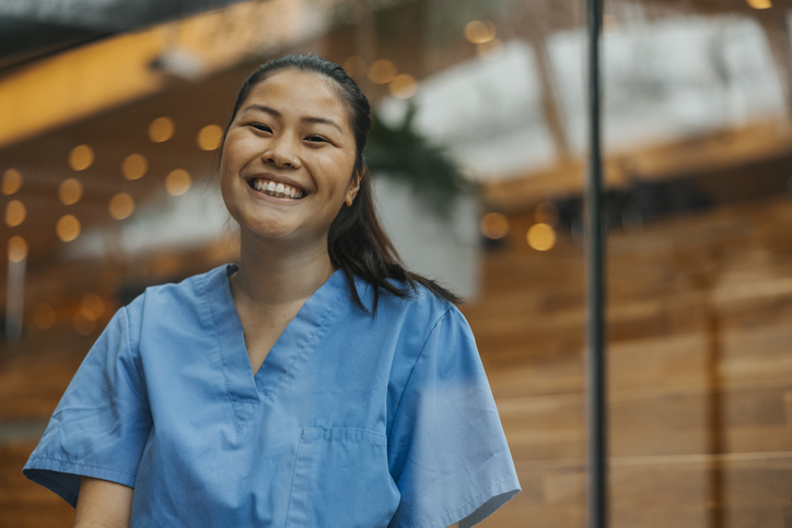 Portrait of happy young female physician in hospital seen through glass