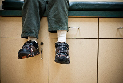 Person sitting on a cabinet edge with feet dangling, wearing dark sneakers and white socks over light-colored cabinetry.