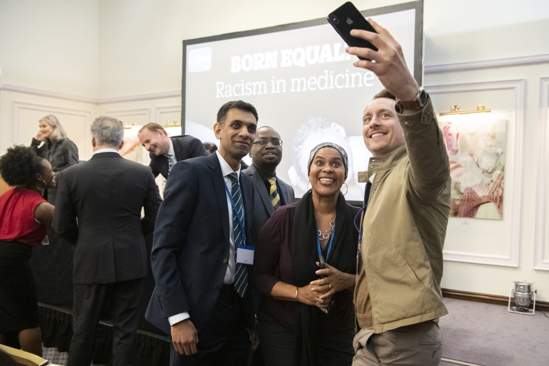 Group of diverse professionals taking a selfie at a conference in front of a poster reading 'Racism in medicine'