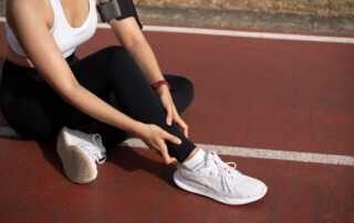 Athlete sits on a red running track, adjusting her black leggings near a white sneaker with a red wristband on her arm.